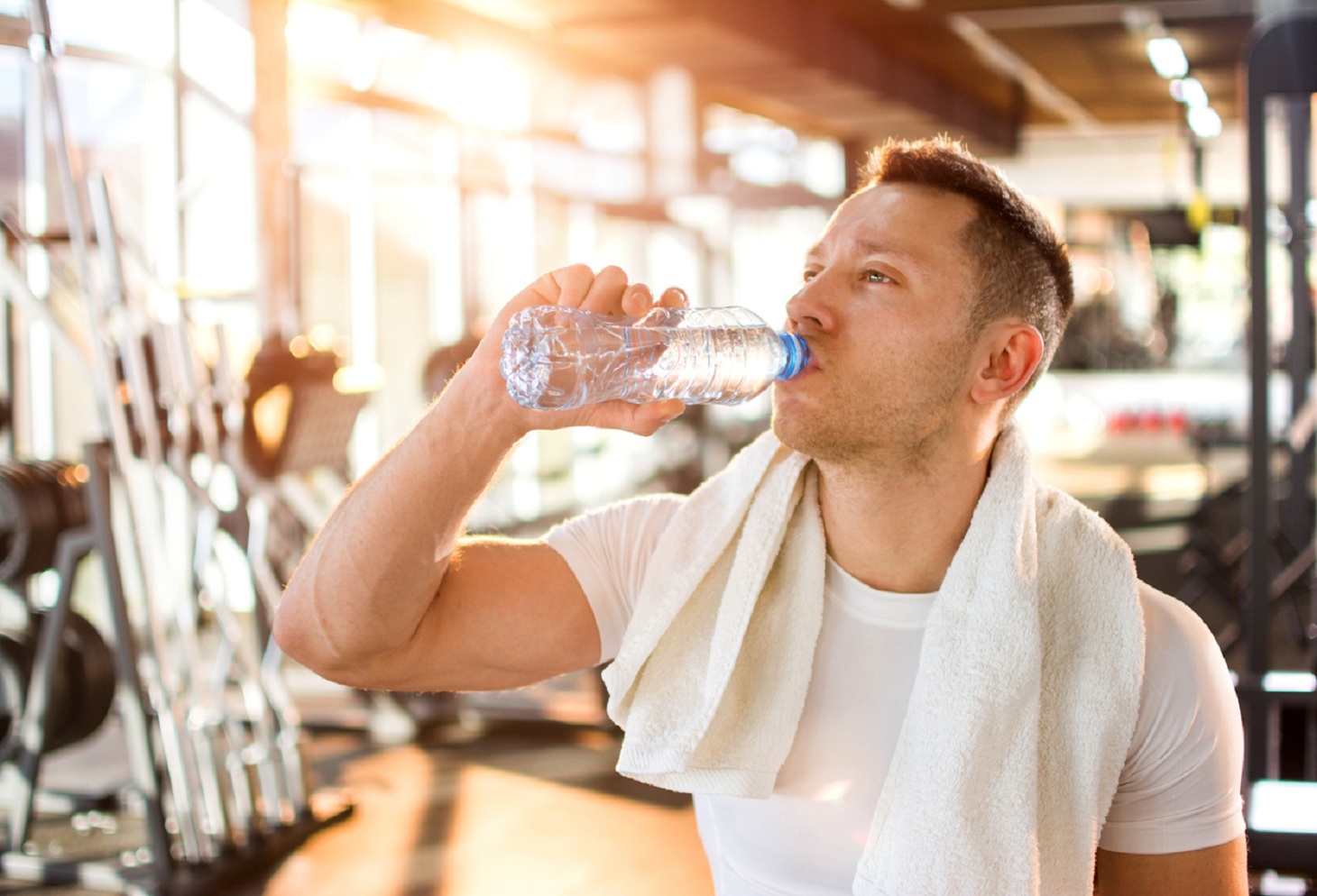 Portrait of young handsome man drinking water in a gym.