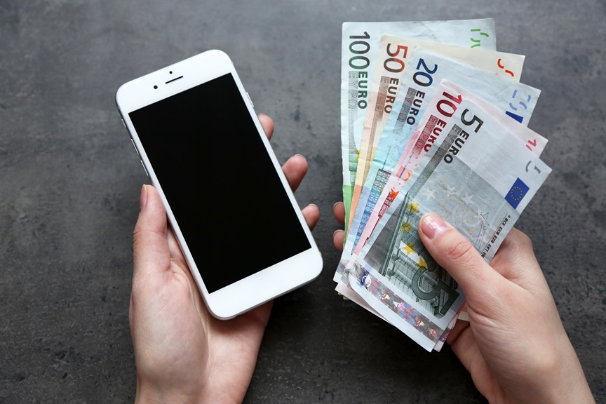 Hands holding smart phone with euro banknotes on grey background. Making money online