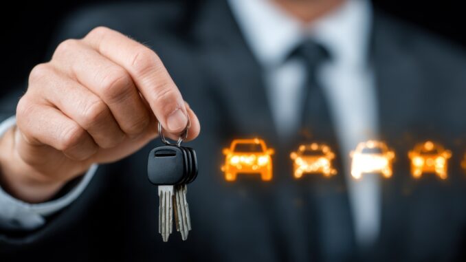 A man in a suit holds car keys with illuminated car icons in the background, symbolizing car sales, rental, or leasing.