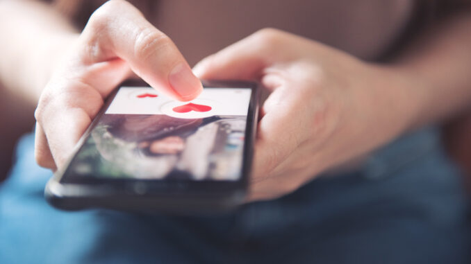 Finger of woman pushing heart icon on screen in mobile smartphon