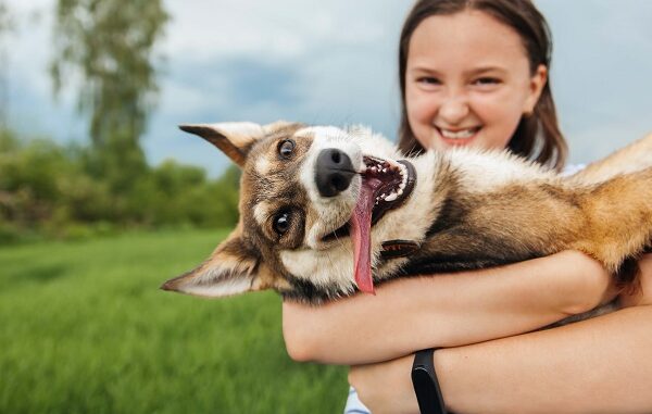 Smiling teenage girl holding a happy dog in her arms, looking at the camera